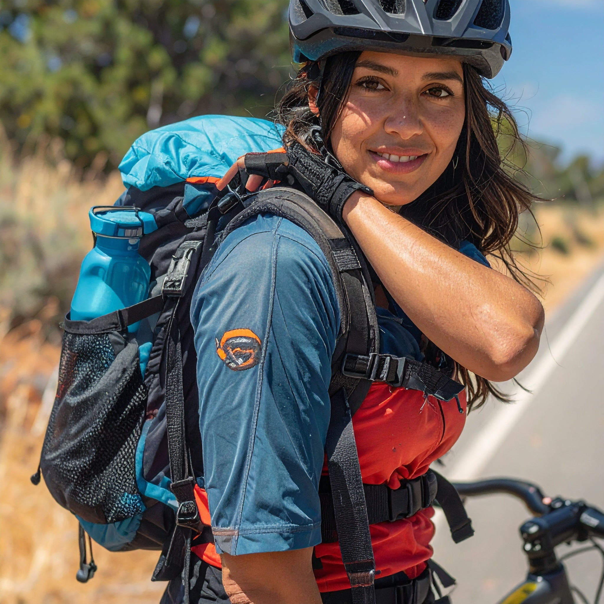 Person wearing a backpack and helmet outdoors, with a bicycle in the background